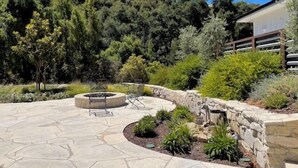 A patio with stone flooring, a fire pit, and surrounding greenery.