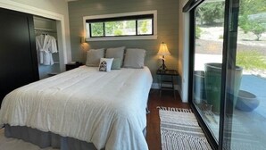 A bedroom with a large bed, a nightstand with a lamp, a window with a view, and a ceiling fan.
