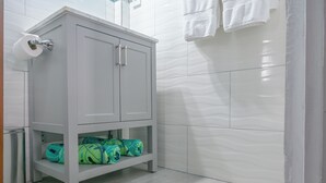 Ein Badezimmer mit einem weißen Schrank, einem Toilettenpapierhalter und einem Regal mit Taschen.