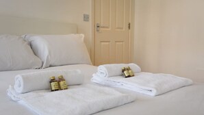 Un lit bien fait, avec des draps blancs, deux flacons de lotion et une porte fermée en arrière-plan.