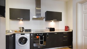 Une cuisine compacte équipée d’un lave-linge, d’un four et d’une machine à café.
