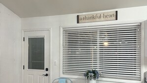 A room with a white door, a window with blinds, two light blue chairs, a small round table with a vase, and a sign above the window reading "a thankful heart". - Family Getaway! Book this home w/ 3 bedrooms/8 beds near Park City! (Heber City)