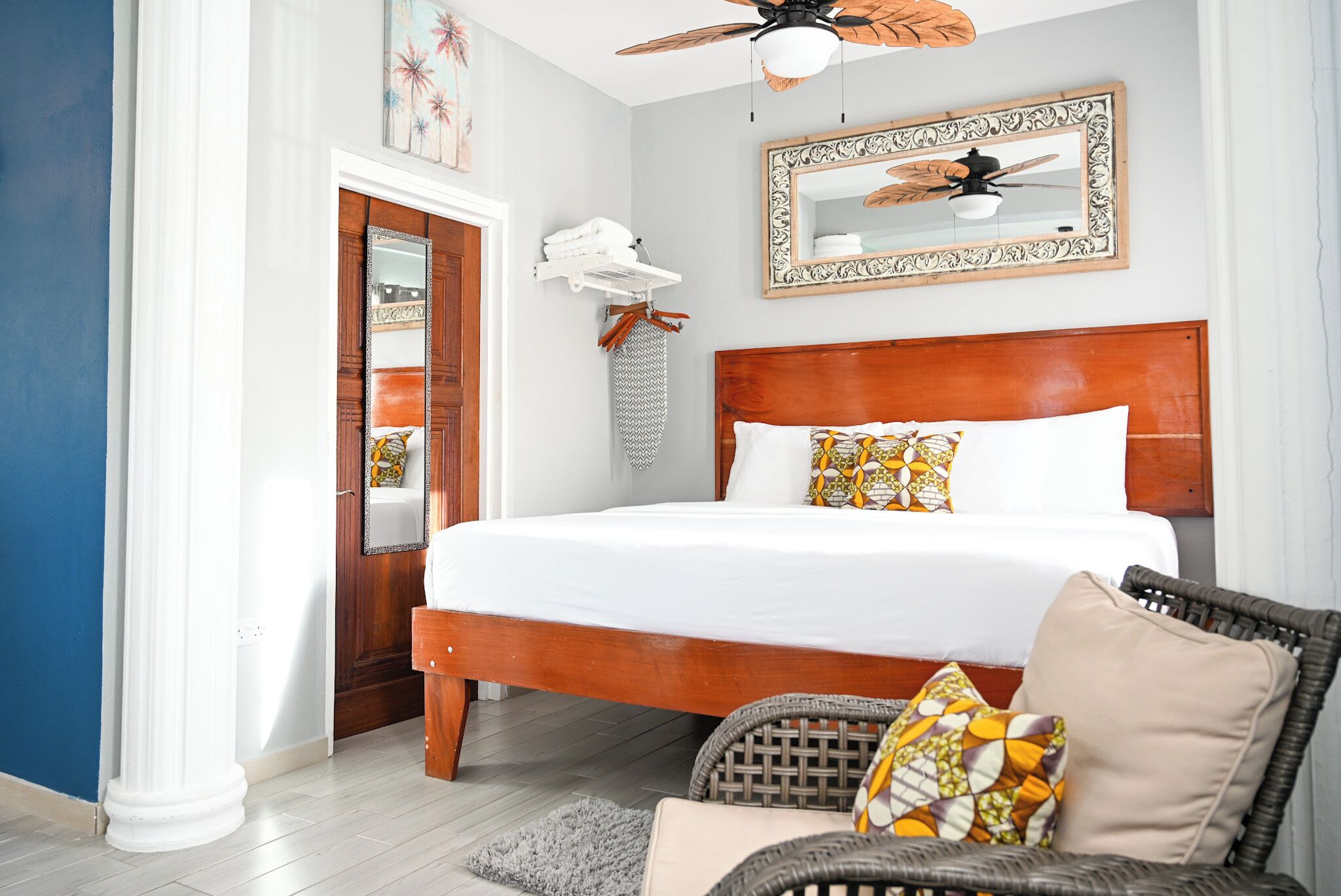 A bedroom with a wooden bed, a ceiling fan, a mirror, and a wicker chair.
