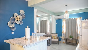 A modern kitchen with a marble countertop, a central island, and a dining area with a chair and table. - Ocean Villa (Corinth)
