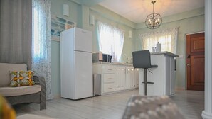 A modern kitchen with white cabinets, a refrigerator, a microwave, and a bar area with a chair. - Ocean Villa (Corinth)