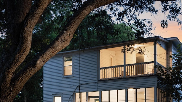 A two-story house with a balcony, surrounded by trees.