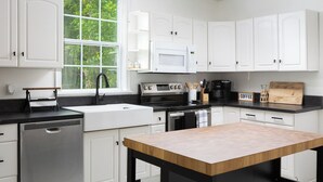 A modern kitchen with white cabinets, a black countertop, a wooden table, and a window with a view of greenery.