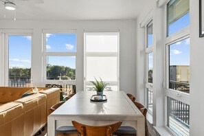 Un comedor moderno con una mesa blanca, sofá de cuero marrón y ventanas amplias con vistas al exterior.