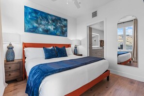 Un dormitorio con una cama grande, una mesita de noche, un espejo y vistas al exterior.