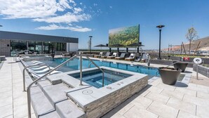 A rooftop pool area with lounge chairs, a hot tub, and a large screen displaying a nature scene. - Superb NEW 2BR amazing amenities (Salt Lake City)