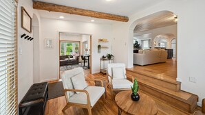 Uma sala de estar ampla com piso de madeira, móveis brancos e uma mesa redonda central.