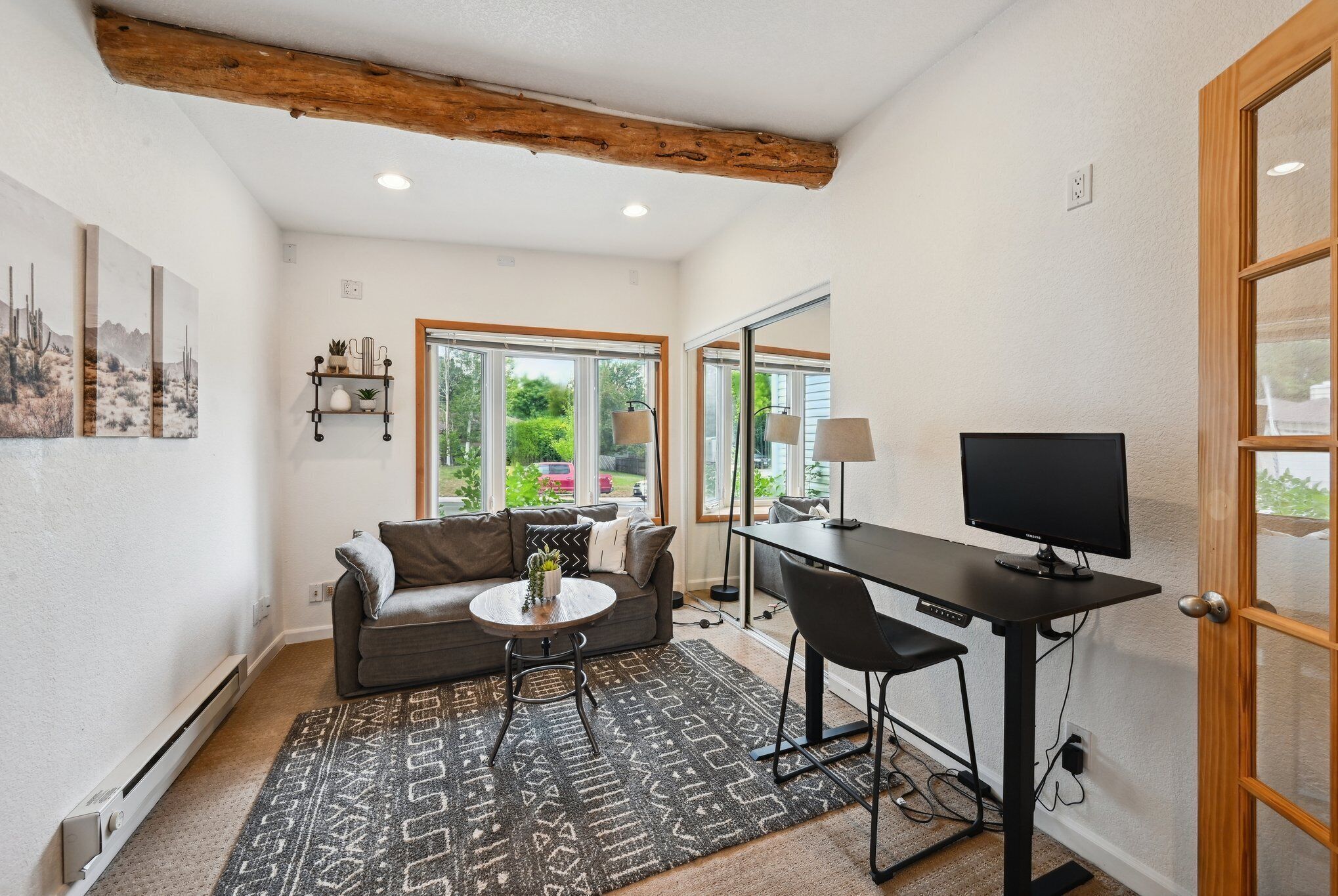 A living room with a sofa, coffee table, and TV, a dining area with a table and chairs, and large windows with a view of greenery.
