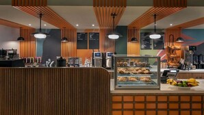 Ein modernes Café mit Holzvertäfelung, einer Theke mit Gebäck und Früchten sowie einer Speisekarte.