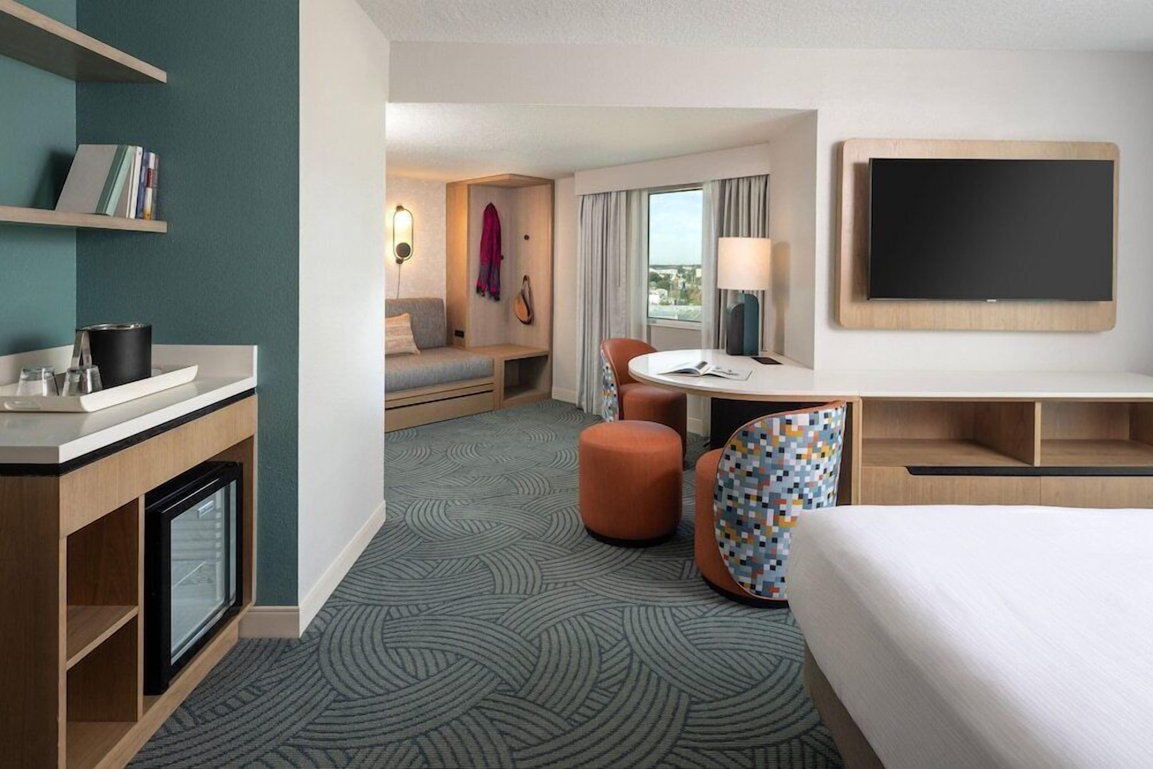 A hotel room with a bed, a desk, a chair, a TV, a small table, and a sofa.