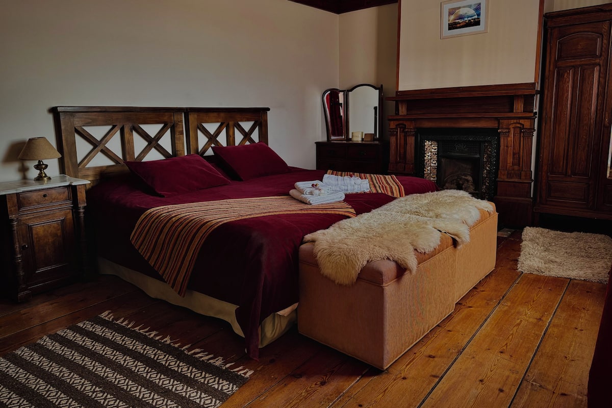 Ein traditionell eingerichtetes Schlafzimmer mit einem hölzernen Bett, einem Kamin, einem Nachttisch und einem gemusterten Teppich.