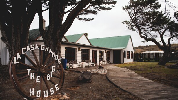 Une maison de campagne avec une grande enseigne en forme de roue en bois sur laquelle on peut lire : « Casa Grande, la grande maison ».