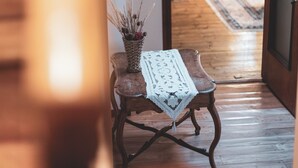 Un couloir avec un plancher en bois, une petite table sur laquelle se trouve un panier en osier et un tissu blanc, et une bibliothèque en arrière-plan.