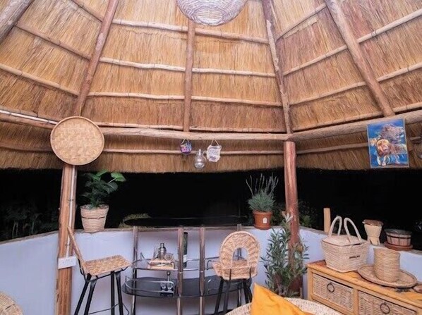 A thatched-roof structure with a dining area, chairs, and potted plants.