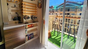 A balcony with a view of a residential building, a wooden shelf with books, and a clock on the wall. - Studio - Sleeps 4 - Pets - Smoking - Wifi (Baguio)