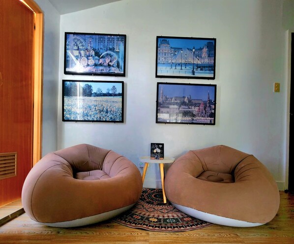 A room with two bean bag chairs, a small table with a picture, and four framed pictures on the wall.