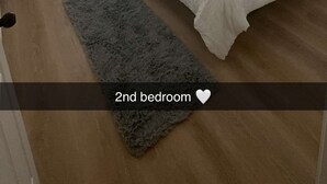 Une deuxième chambre avec un lit, des rideaux, un ventilateur de plafond, une lampe et un tapis.
