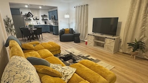 Un salon moderne avec un canapé jaune, un téléviseur à écran plat et un ventilateur de plafond.
