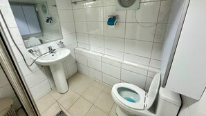 Een badkamer met een wit wastafelmeubel, toilet, spiegel en ventilatie.