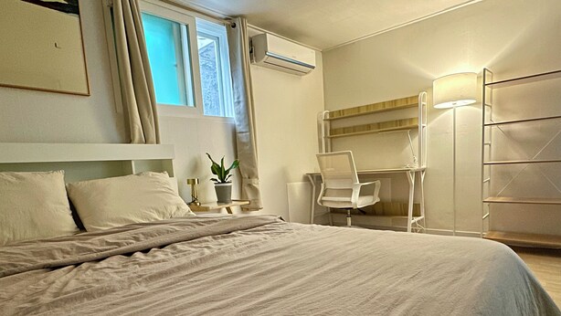 Een slaapkamer met een groot bed, een bureau, een stoel en een wandplank.