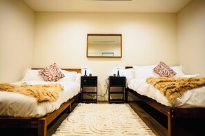 Two single beds with white linens and decorative pillows, each with a bedside table and lamp.