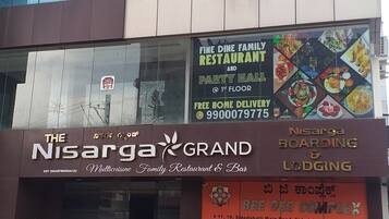 A building with multiple floors, including a ground floor with a restaurant named 'Nisarga Grand' and a sign for 'Bee Gee Complex' above.