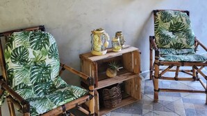 Ein Zimmer mit zwei Bambusstühlen, einem Holzregal mit Topfpflanzen und einem gefliesten Boden.