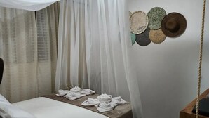 Ein Bett mit weißer Bettwäsche, eine hölzerne Bank und eine Wand mit gewebten Hüten.