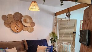 Ein gemütlicher Wohnbereich mit einer Couch, einem Hängekorbstuhl und einer Wand, die mit gewebten Dekorationen verziert ist.