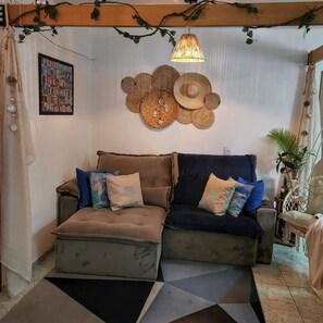 A cozy living area with a sofa set, decorative wall hangings, and a hanging light fixture.