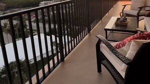 A balcony with a view of the sunset over a body of water, equipped with outdoor furniture.