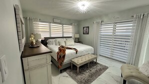 A bedroom with a large bed, a bedside table, a bench, a dresser, and a mirror.