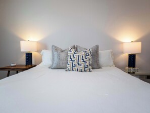 A neatly made bed with white linens, two bedside tables with lamps, and decorative pillows.