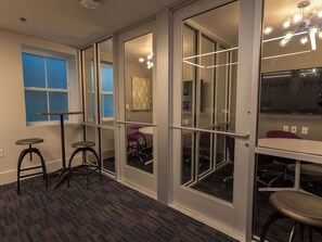 A modern office space with glass partitions, a desk, two stools, and a ceiling light fixture.