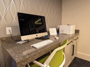 A hotel workspace with a desktop computer, keyboard, mouse, and printer on a granite countertop.