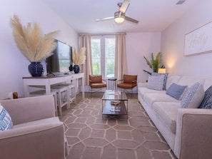 A living room with a sofa, chairs, a coffee table, a TV, and a ceiling fan. - Golding Era at 514 Jackson (Oxford)