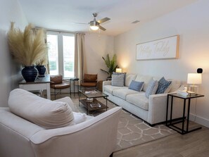 A living room with a white sofa, a brown armchair, a glass coffee table, and a ceiling fan.