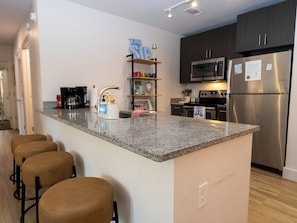 A modern kitchen with granite countertops, stainless steel appliances, and a bar area with stools. - Golding Era at 514 Jackson (Oxford)