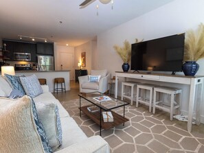 A modern living room with a sofa, coffee table, TV, kitchen area, and a dining table. - Golding Era at 514 Jackson (Oxford)