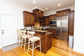 Una cocina con gabinetes de madera, un refrigerador de acero inoxidable y una zona de bar con taburetes.