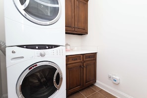 Un cuarto de lavandería con lavadora y secadora apiladas, armarios de madera y una encimera.