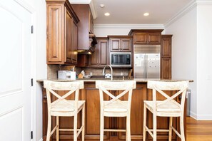 A kitchen with wooden cabinets, a stainless steel refrigerator, and a bar area with two stools.