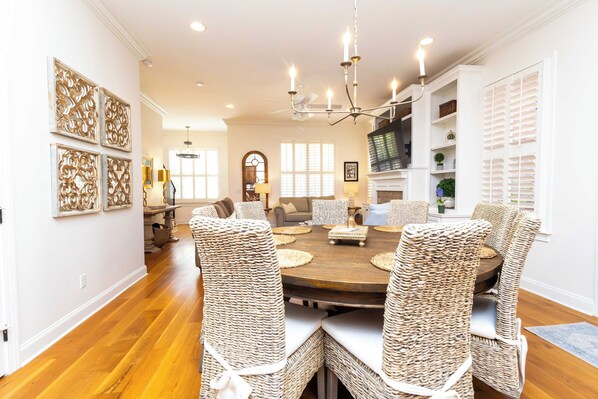 A dining room with a round table, wicker chairs, and a chandelier.