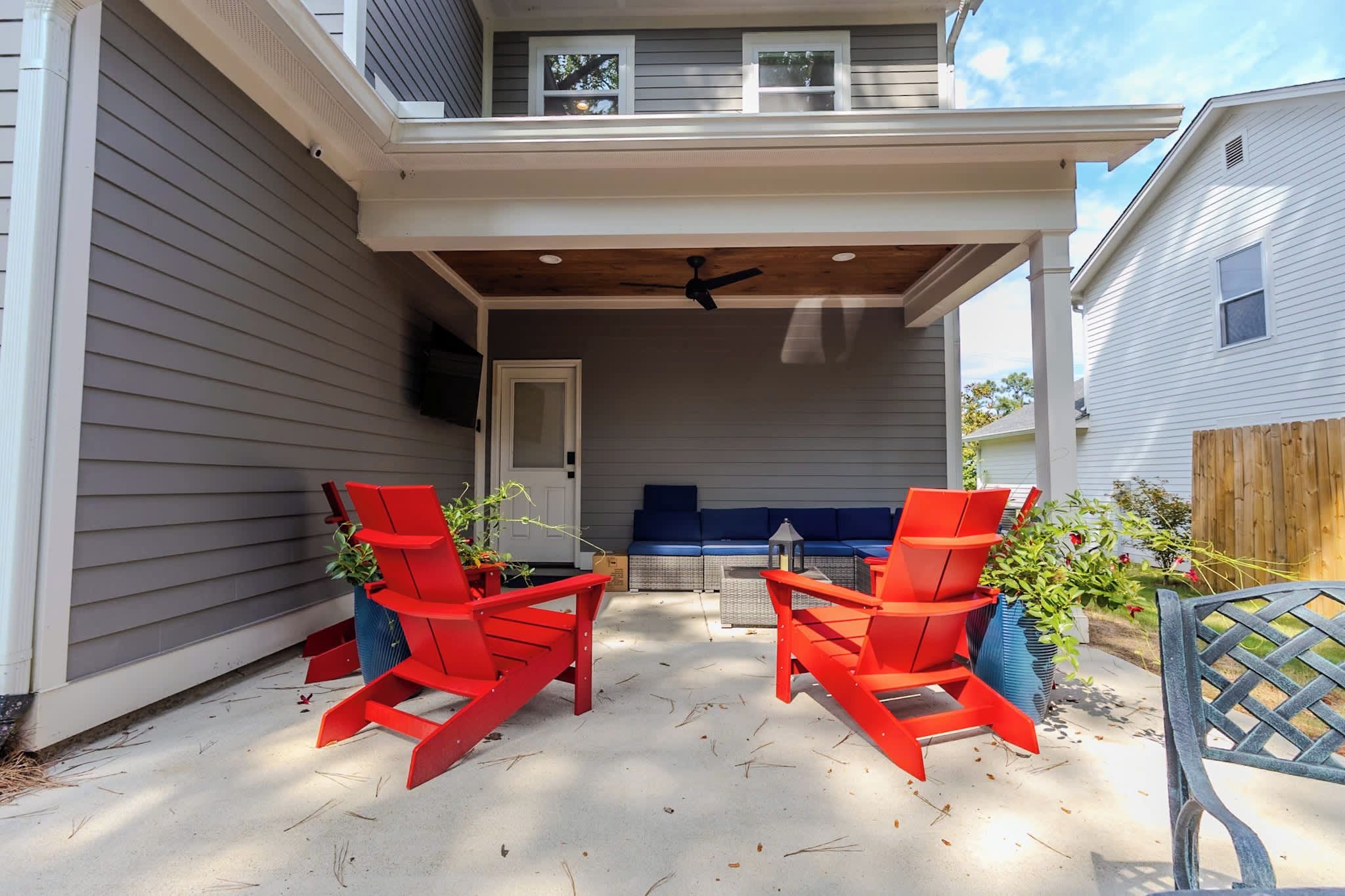 A covered patio area with two red chairs and a table, a ceiling fan, and a view of the house.