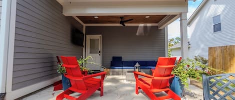 A covered patio area with two red chairs and a table, a ceiling fan, and a view of the house.