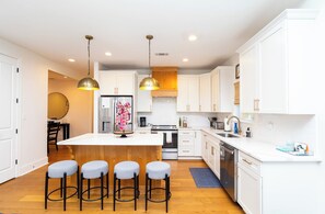 A modern kitchen with white cabinets, a central island with stools, stainless steel appliances, and pendant lighting. - Sip Sanctuary by Apex Short Term Stays (Oxford)